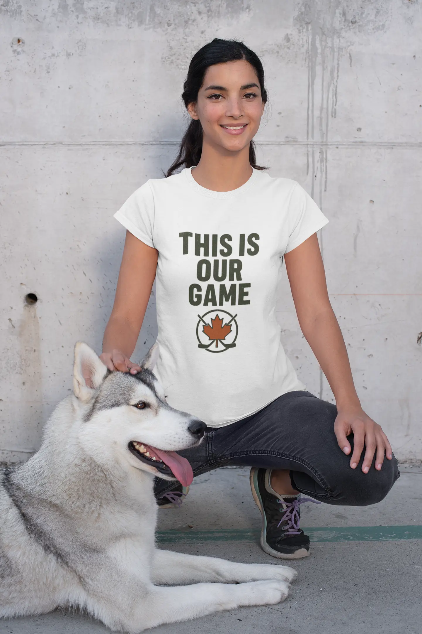 Girl wearing white 'This Is Our Game' youth T-shirt with maple leaf graphic, sitting next to a husky dog – Maple Stick Hockey product.