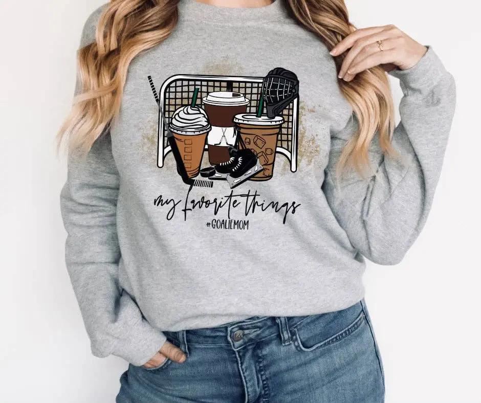 Woman wearing grey 'Goalie Mom' crewneck sweatshirt with 'My favourite things' graphic featuring coffee cups, skates and hockey gear – Maple Stick Hockey product.